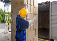 Person in blue overalls and yellow hard hat unloading cardboard boxes from a shipping container.