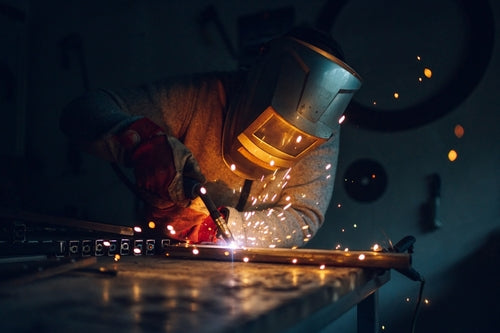 Person welding metal with sparks flying in a dark workshop setting