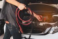 Person holding jump leads next to an open car hood